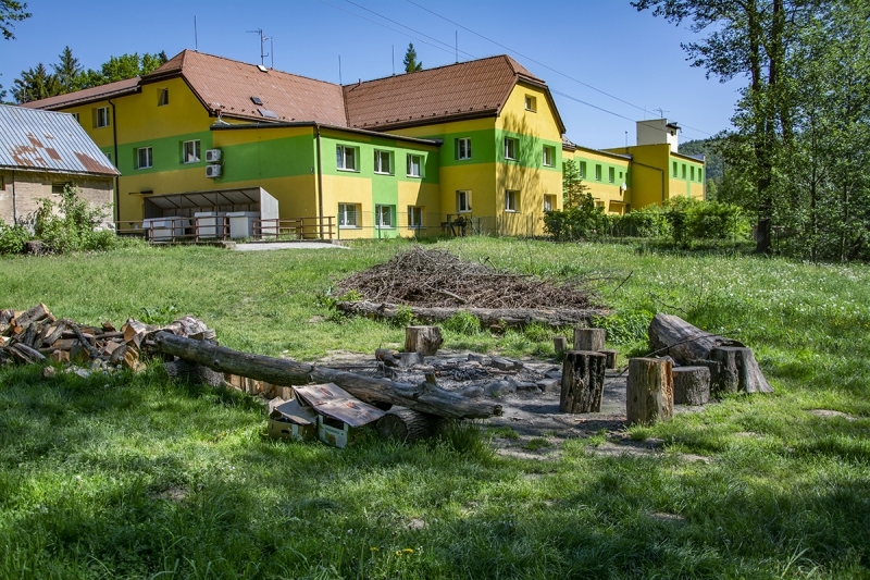 Budova školy s ohništěm a posezením uprostřed zeleně